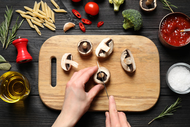 Photo of Woman cutting mushrooms at black wooden table, top view. Healthy cooking