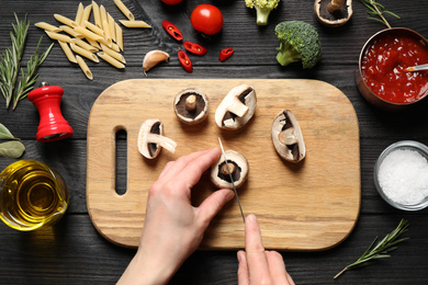 Woman cutting mushrooms at black wooden table, top view. Healthy cooking