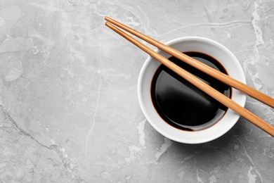 Photo of Bowl of soy sauce with chopsticks on marble background, top view. Space for text