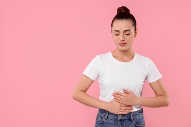 Photo of Woman suffering from abdominal pain on pink background, space for text. Unhealthy stomach