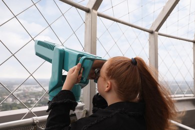 Photo of Teenage girl looking through tower viewer at city