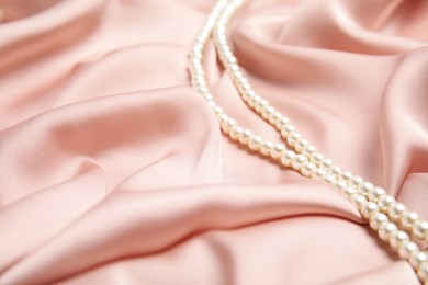 Photo of Beautiful pearls on pink silk, space for text