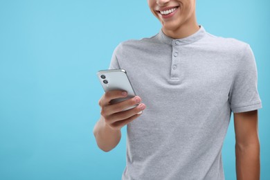 Young man sending message via smartphone on light blue background, closeup. Space for text