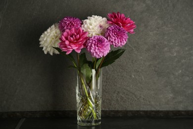 Bouquet of beautiful Dahlia flowers in vase on black table near dark grey textured wall