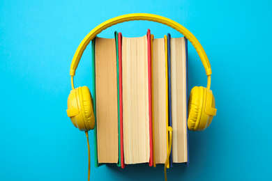 Photo of Books and modern headphones on light blue background, top view