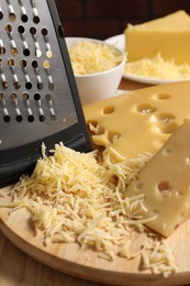 Photo of Grated, cut cheese and grater on wooden table, closeup