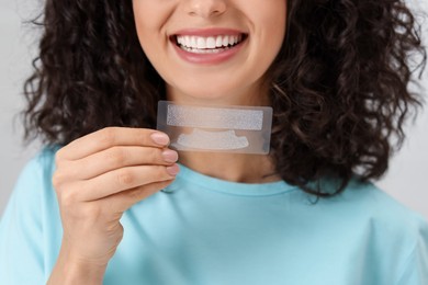 Photo of Young woman holding teeth whitening strips on light background, closeup