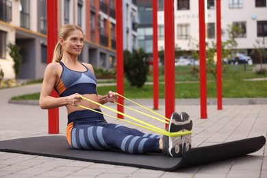 Photo of Athletic woman doing exercise with fitness elastic band on mat at outdoor gym