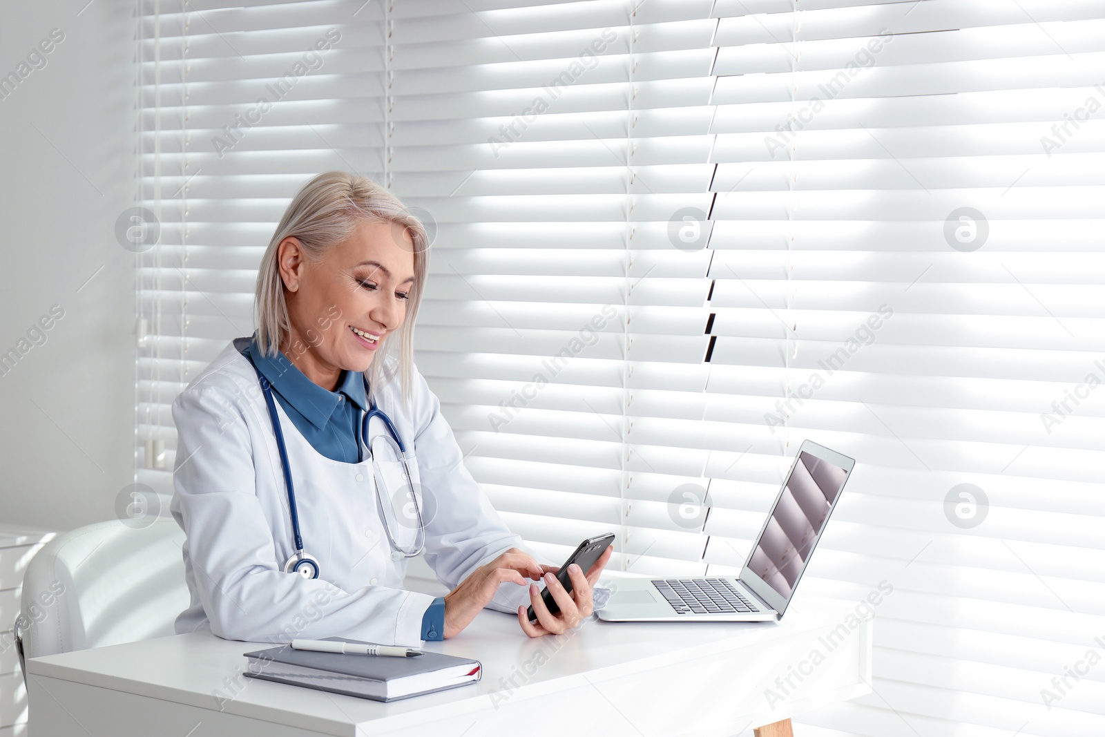 Photo of Mature female doctor with smartphone at table in office