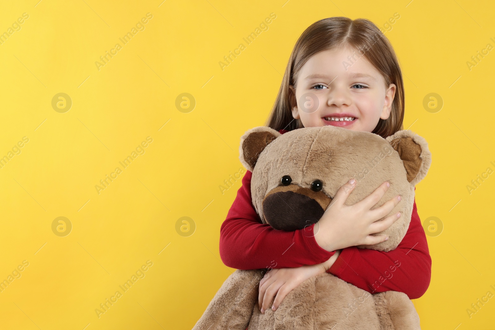Photo of Cute little girl with teddy bear on yellow background. Space for text