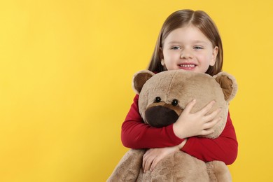 Cute little girl with teddy bear on yellow background. Space for text