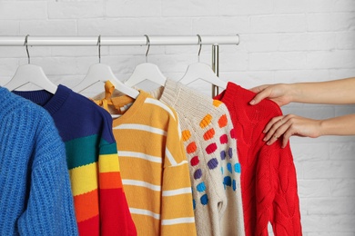 Photo of Woman choosing sweater on rack against brick wall