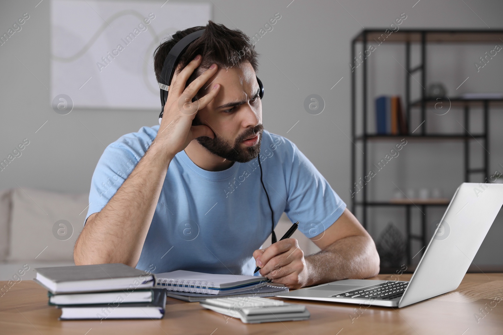 Photo of Confused young man watching webinar at table in room