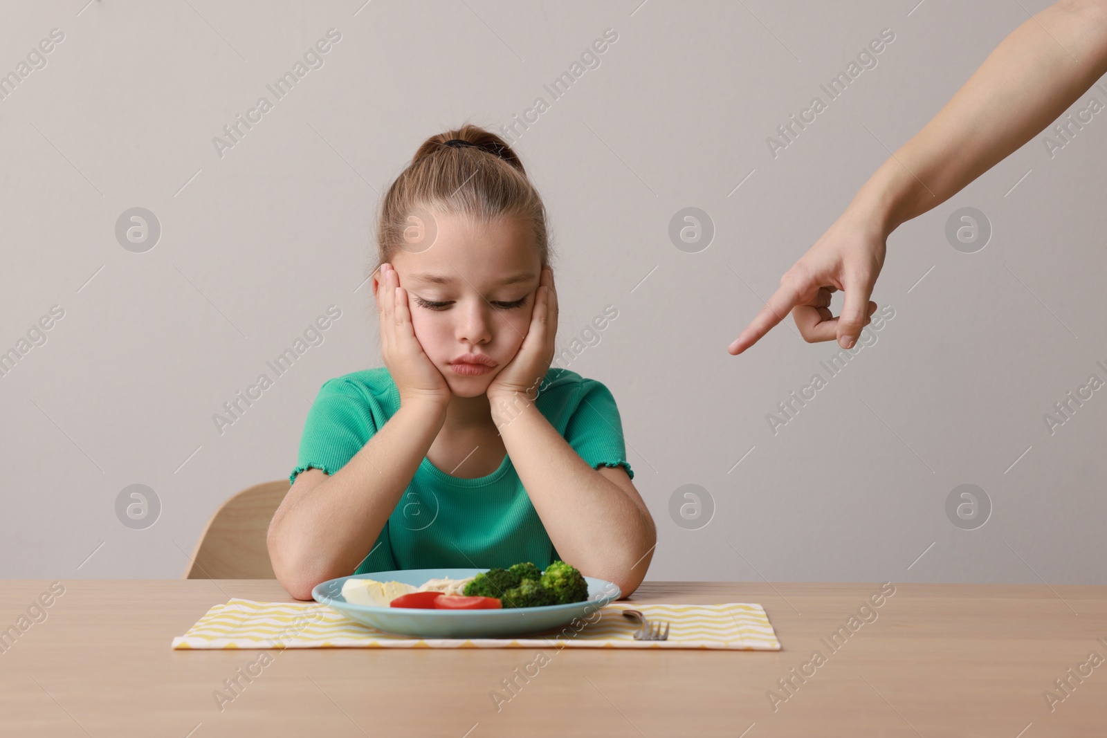 Photo of Cute little girl refusing to eat her breakfast at table on grey background