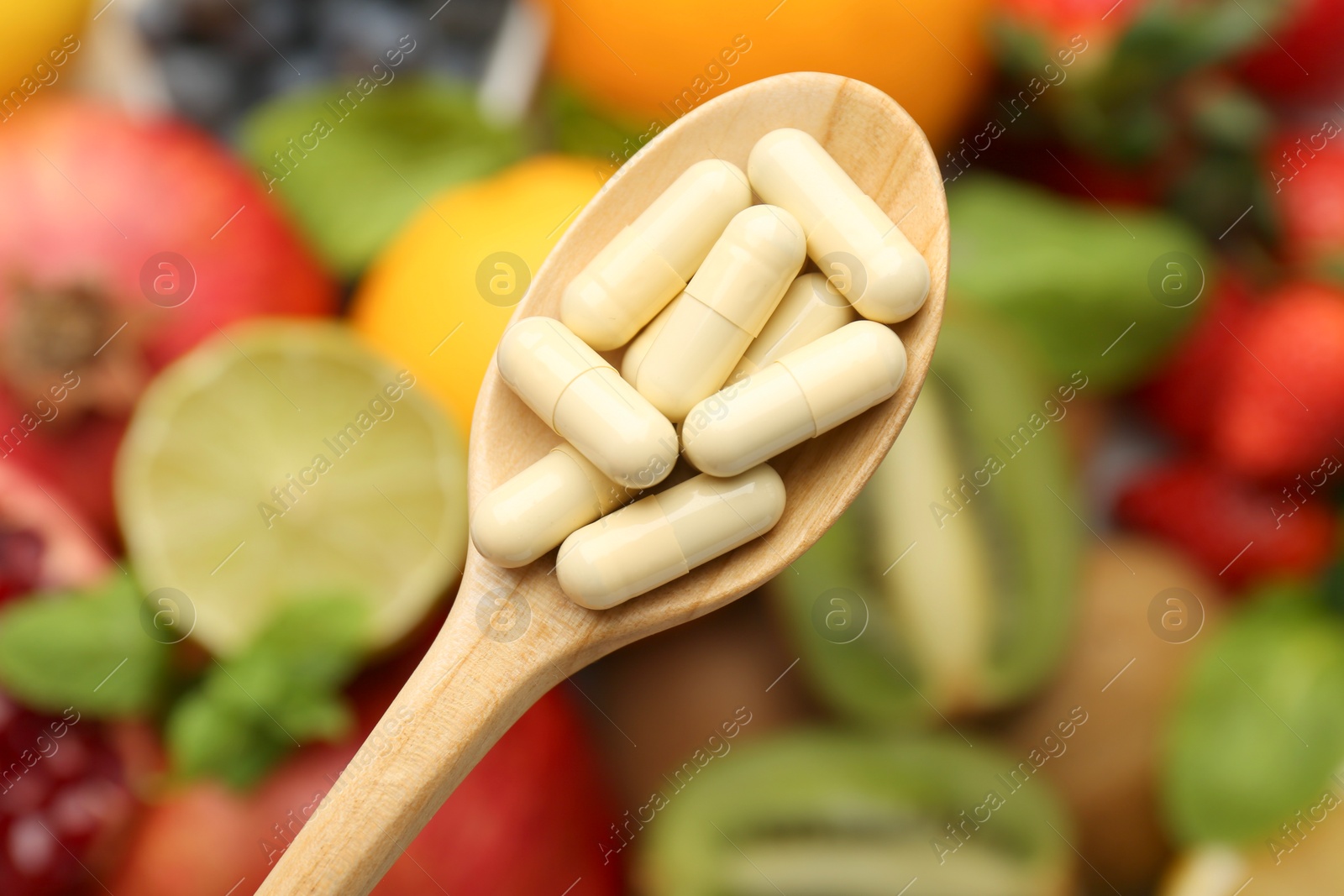 Photo of Vitamin pills in spoon over fresh fruits, top view