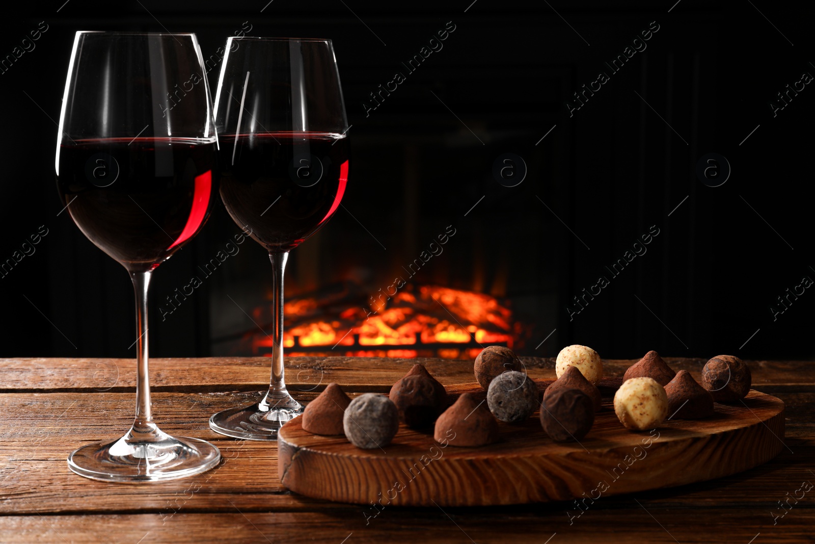 Photo of Red wine and chocolate truffles on wooden table against fireplace