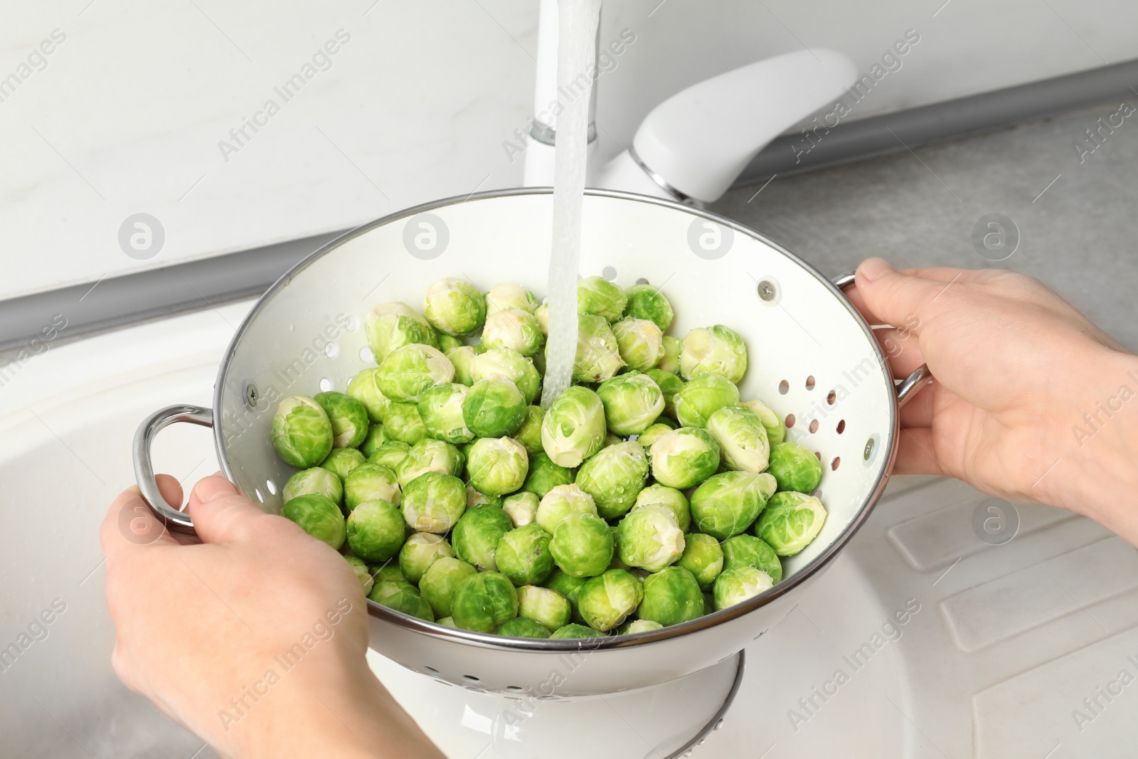 Photo of Woman washing fresh Brussels sprouts in colander, closeup