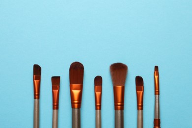 Photo of Set of makeup brushes on light blue background, flat lay. Space for text