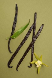 Photo of Vanilla pods, beautiful flower and green leaf on olive color background, top view