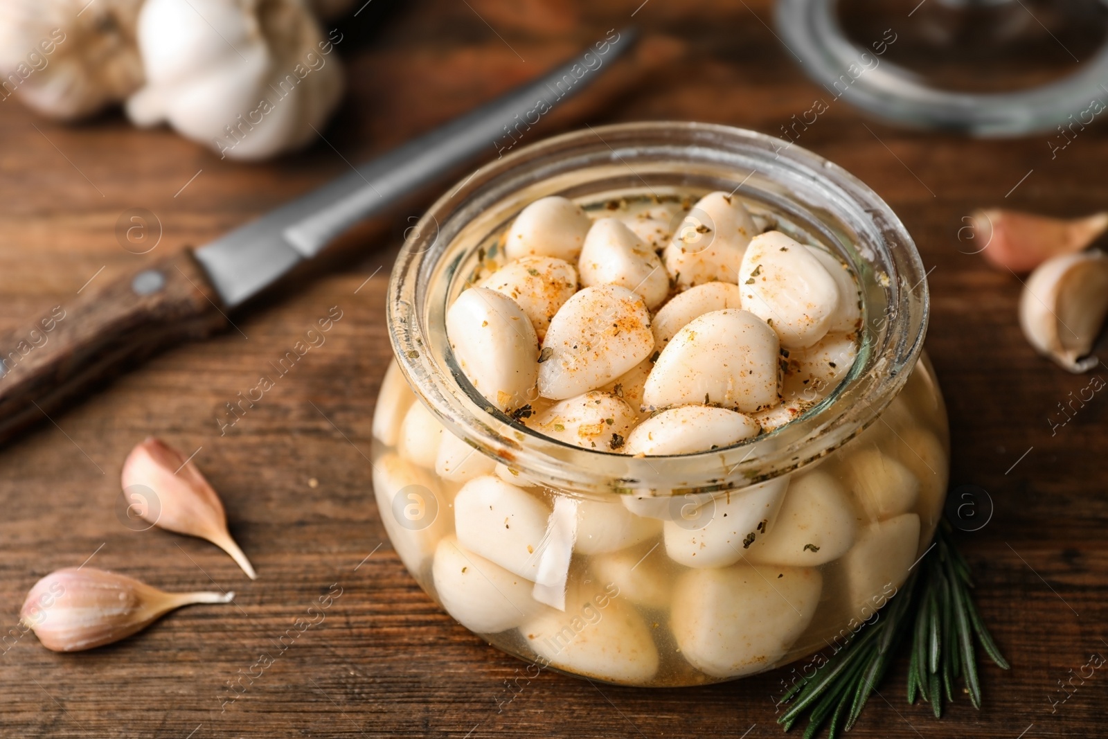 Photo of Preserved garlic in glass jar on wooden table, closeup