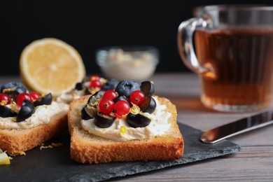 Photo of Tasty sandwiches with cream cheese, blueberries, red currants and lemon zest on wooden table