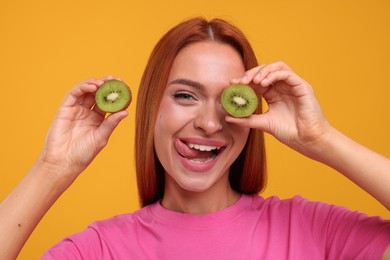 Photo of Funny woman with halves of fresh kiwi showing tongue on orange background