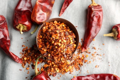 Photo of Bowl with crushed chili pepper and pods on fabric