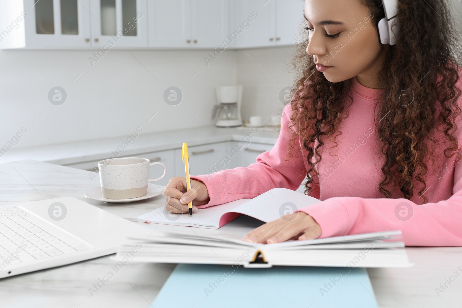 Photo of African American woman with modern laptop and headphones studying in kitchen. Distance learning