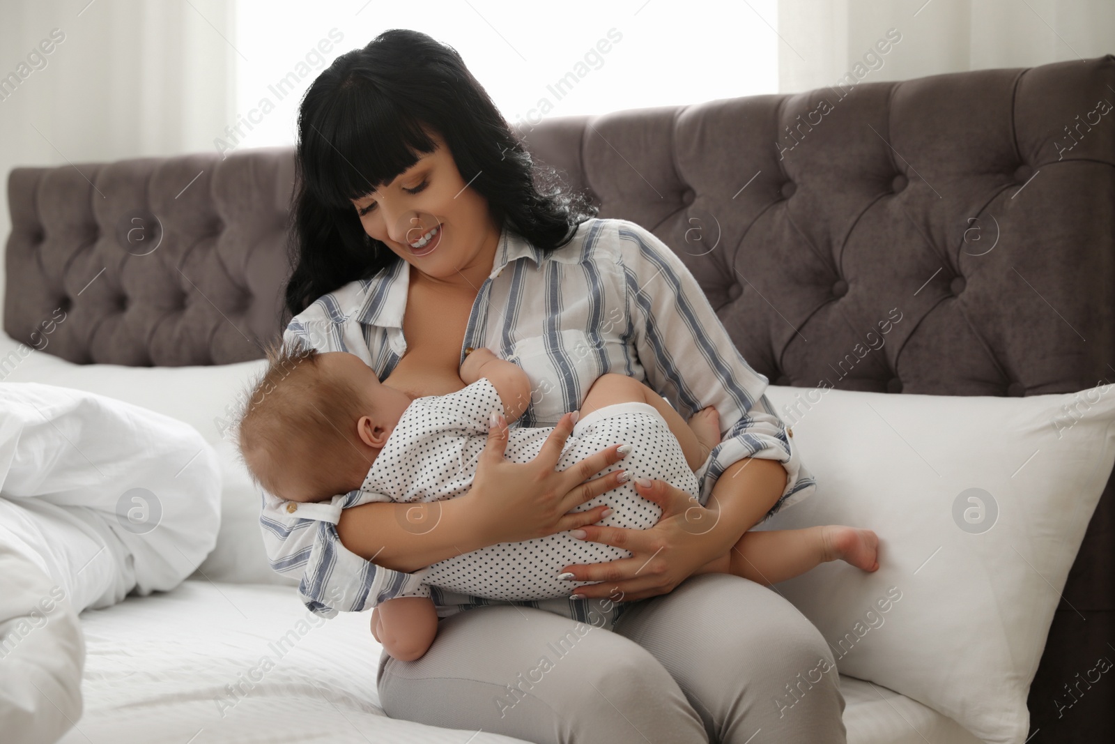 Photo of Woman breastfeeding her little baby on bed indoors