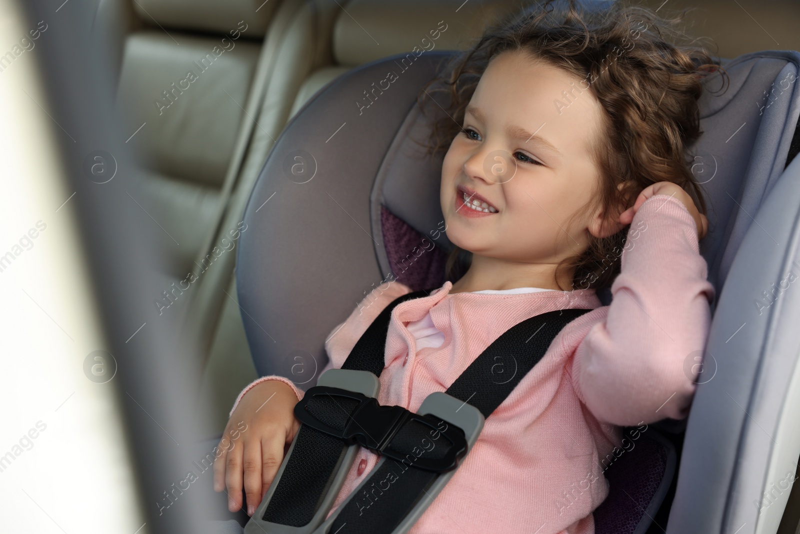 Photo of Cute little girl sitting in child safety seat inside car