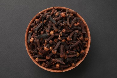 Photo of Aromatic dry cloves in wooden bowl on grey background, top view