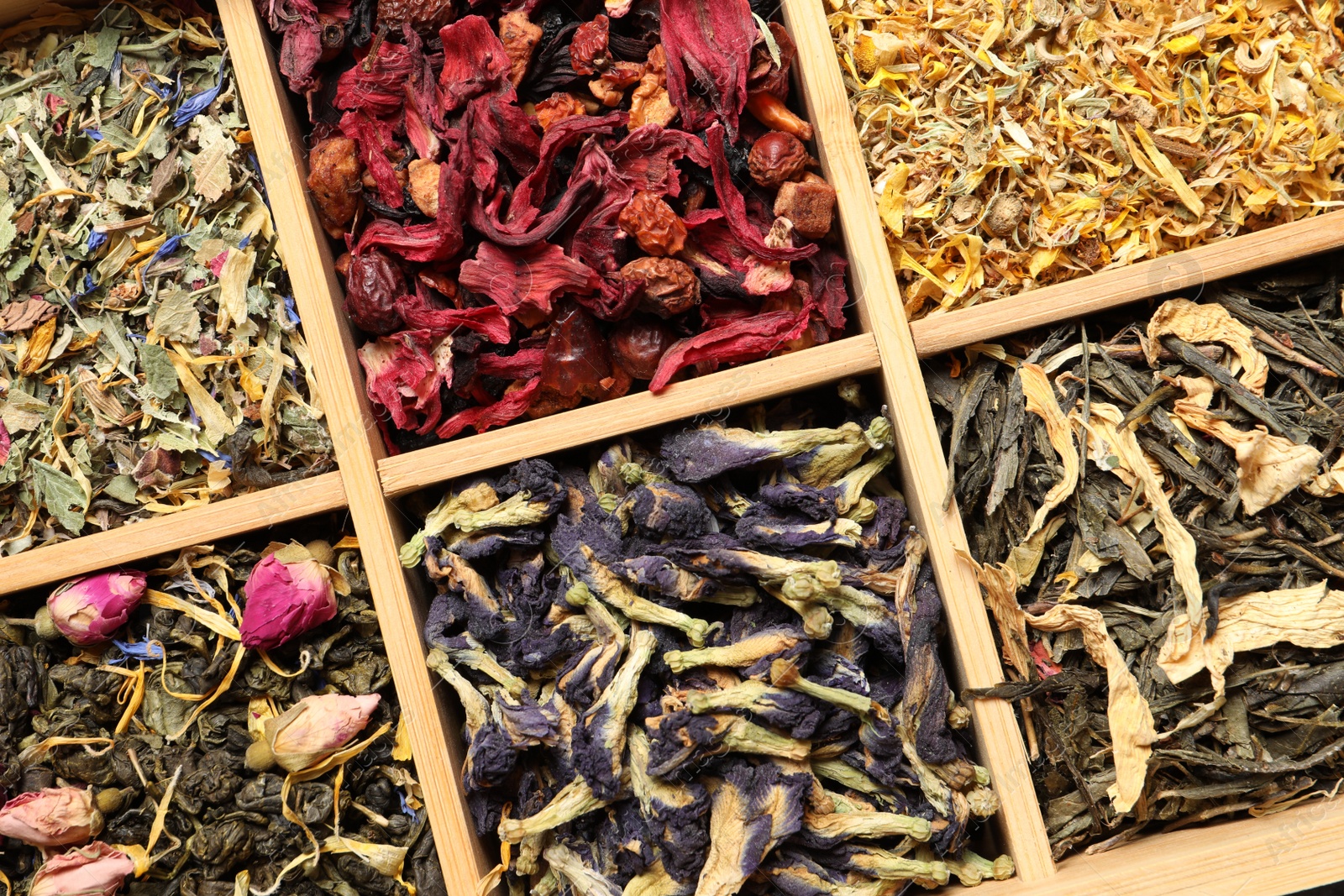 Photo of Different dry herbal teas in wooden box, top view