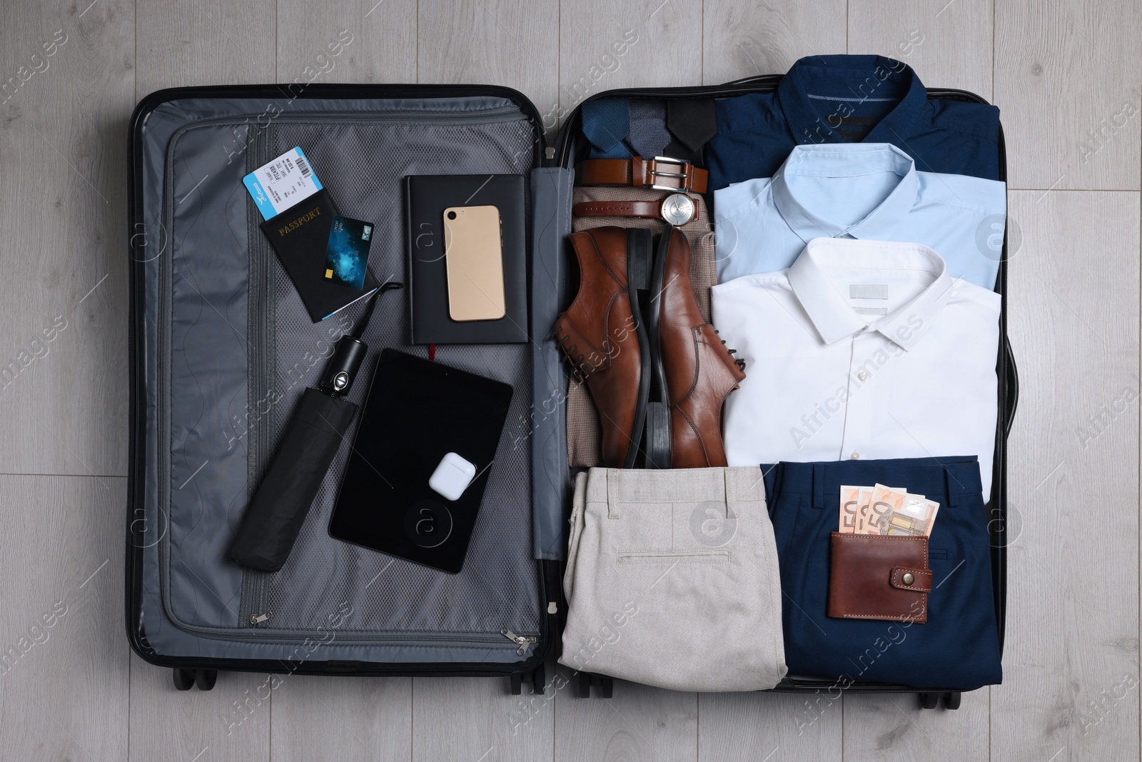 Photo of Folded clothes, shoes and accessories in open suitcase on wooden background, top view. Packing for business trip