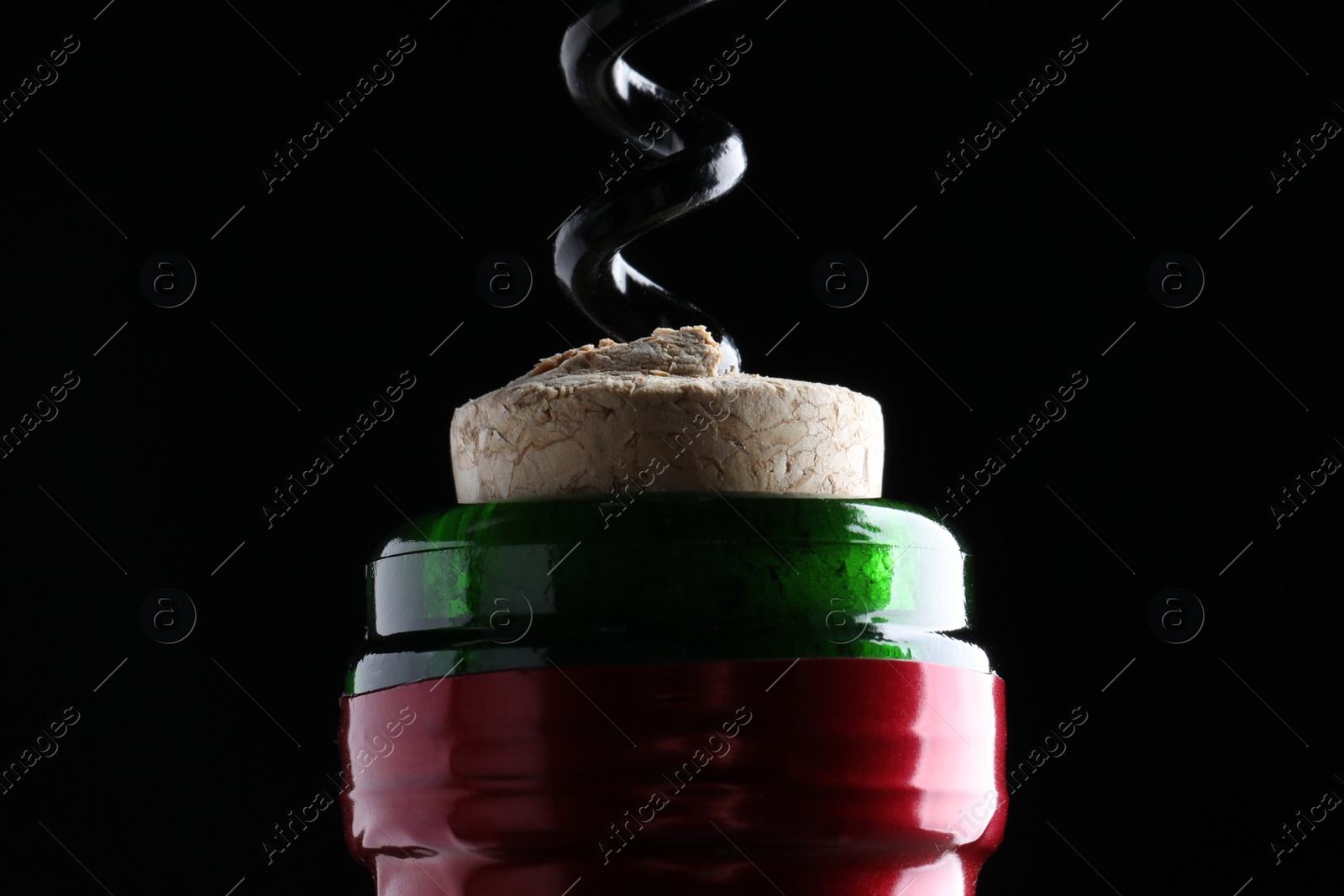 Photo of Opening wine bottle with corkscrew on dark background, closeup
