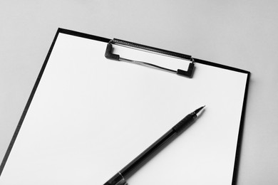 Photo of Black clipboard with sheet of blank paper and pen on light grey background, closeup