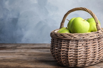 Photo of Wicker basket of fresh ripe green apples on wooden table against blue background, space for text