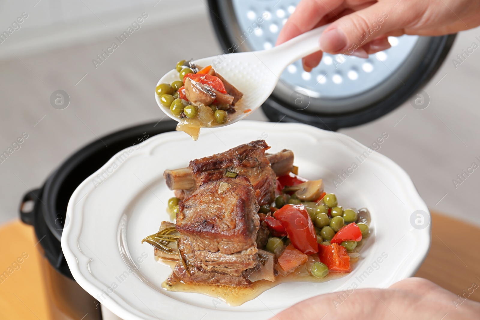 Photo of Woman putting meat and garnish prepared in multi cooker on plate, closeup