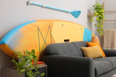 Photo of SUP board, paddle and stylish sofa in living room. Interior design