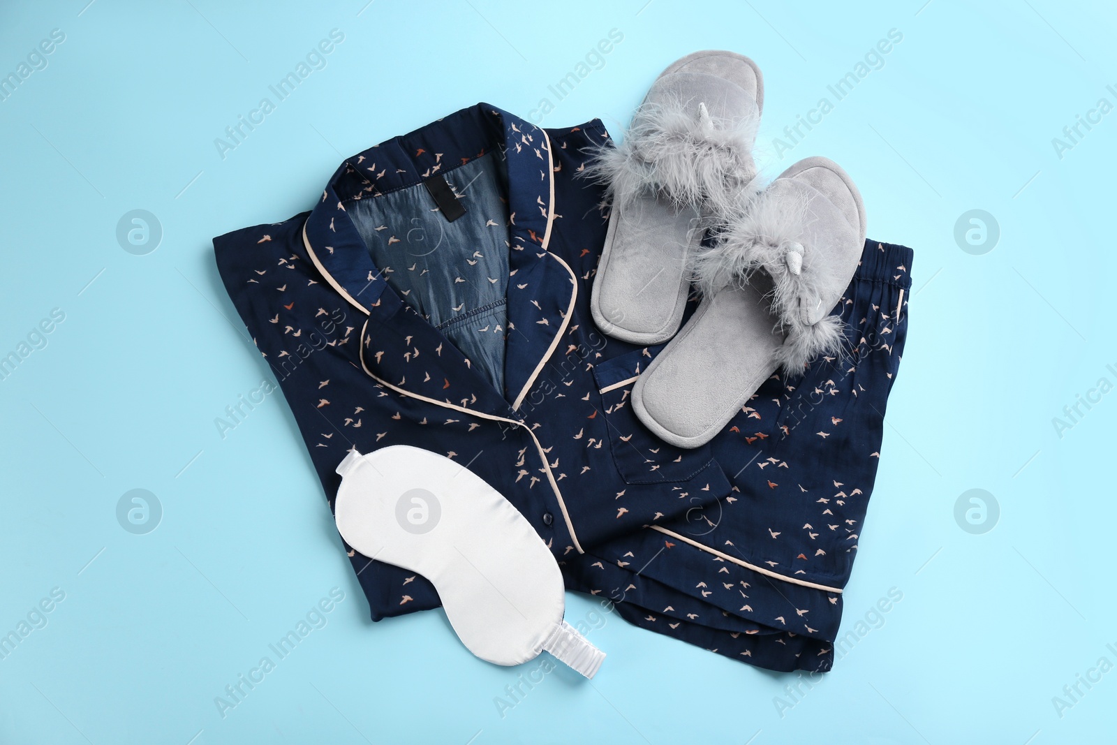 Photo of House slippers, sleeping mask and pajamas on light blue background, flat lay