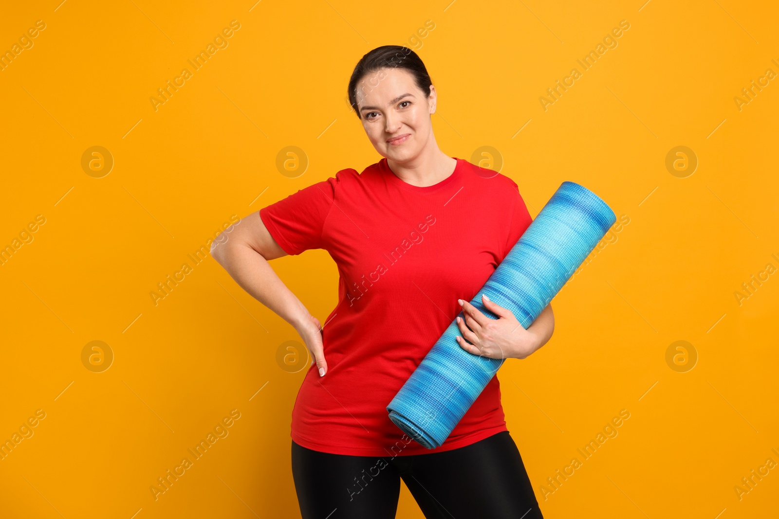 Photo of Happy overweight woman with yoga mat on orange background