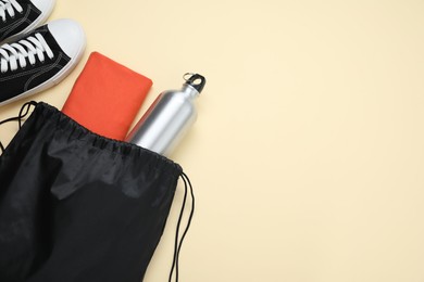 Photo of Black drawstring bag, sneakers, thermo bottle and cloth on beige background, flat lay. Space for text