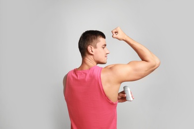 Young man applying deodorant to armpit on light background