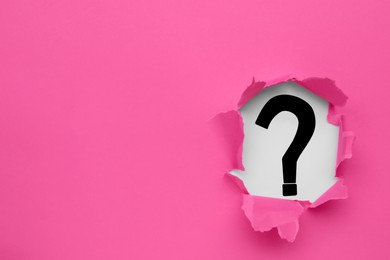 Photo of Question mark on white background, view through hole in pink paper, space for text