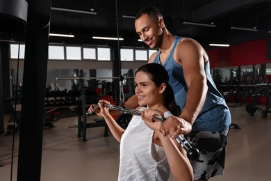 Photo of Happy trainer showing woman how to do exercise properly in modern gym