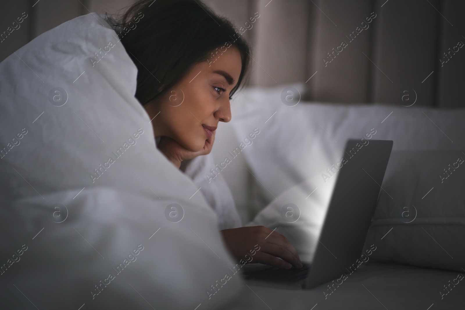 Photo of Young woman with nomophobia using laptop in bed at night. Insomnia concept