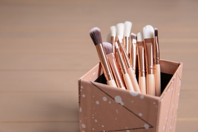 Photo of Organizer with professional makeup brushes on wooden table. Space for text