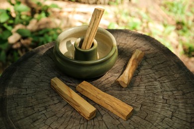 Photo of Palo santo sticks with holder on wooden stump outdoors