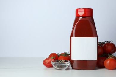 Bottle of tasty ketchup and ingredients on white marble table. Space for text