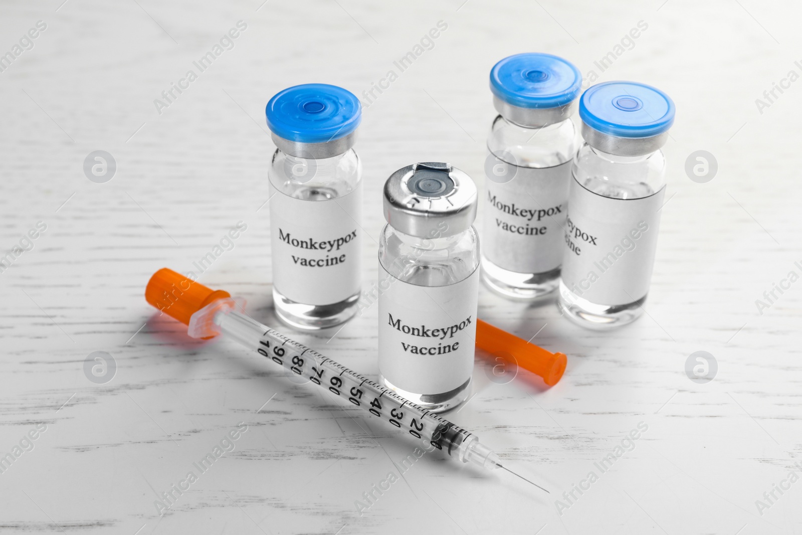 Photo of Monkeypox vaccine in glass vials and syringe on white wooden table