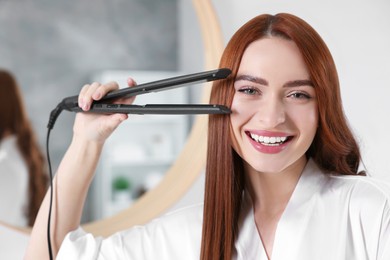 Photo of Beautiful woman with hair iron in room